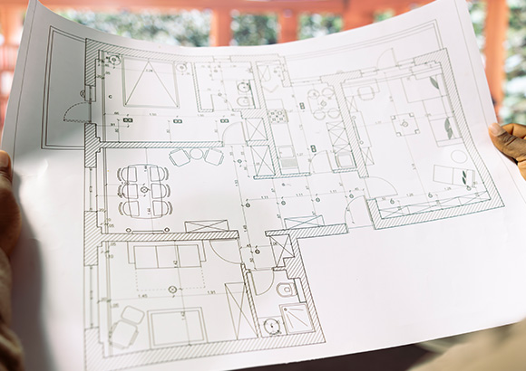 person holding architectural blueprints of a six room house layout with detailed measurements and furniture placements